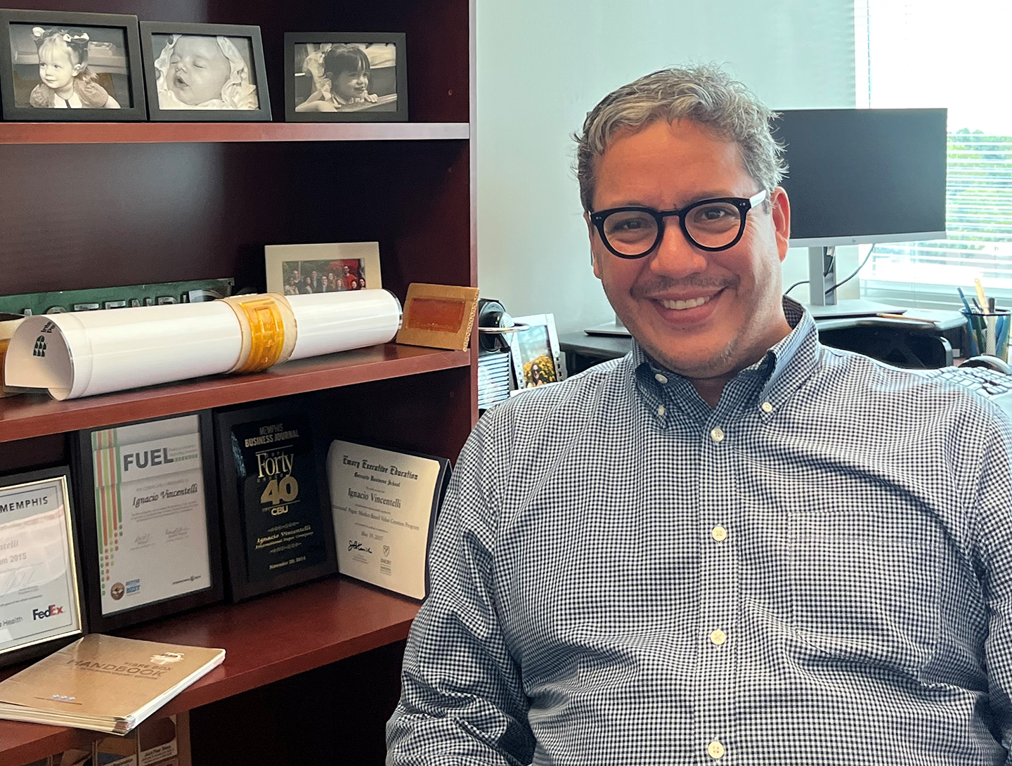 Ignacio smiles at the camera from behind his desk at work with pictures of his kids in the background