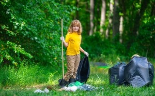 A little girl picks up litter in a park-lilke setting