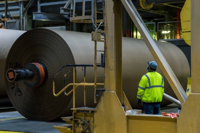 An IP employee surveys a large roll of brown paper coming off the assembly line