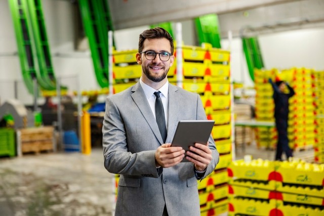 A man in a tie checks a list with food ready to be shipped in the background