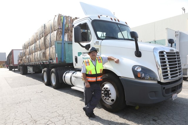 Worker leaning on the cabin of a fully loaded cardboard truck