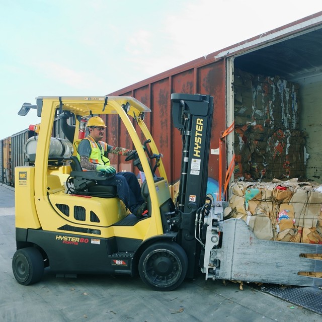 man in a forklift pushing a cardboard bale